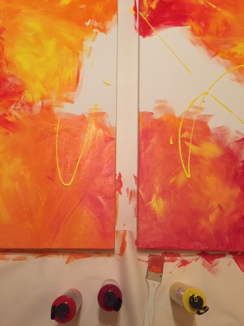 Birdseye view of two canvasses - each one is an abstract painting of swirling colours of yellow, orange, reds.